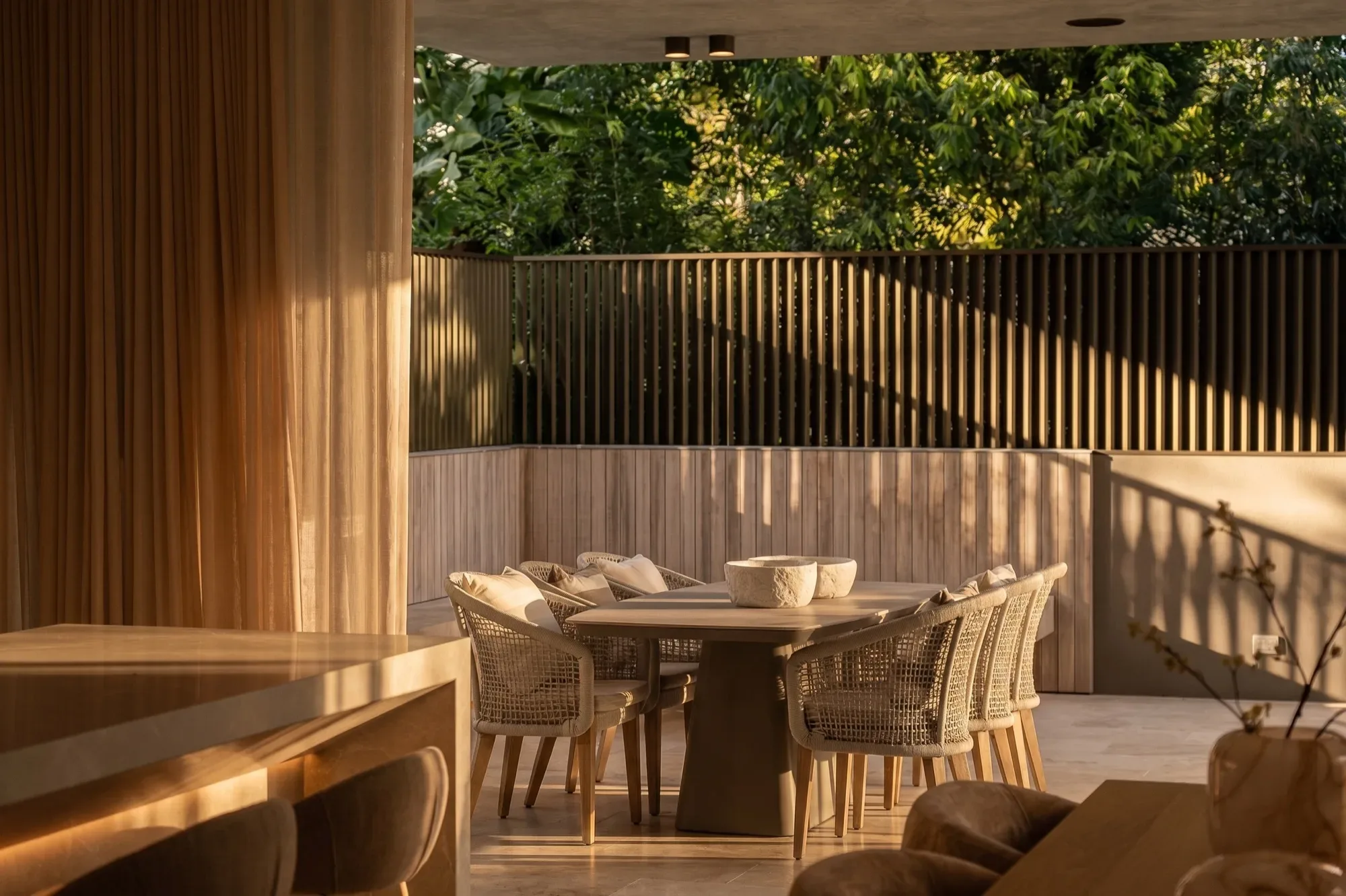 An outdoor dining table under a timber screen, garden beyond