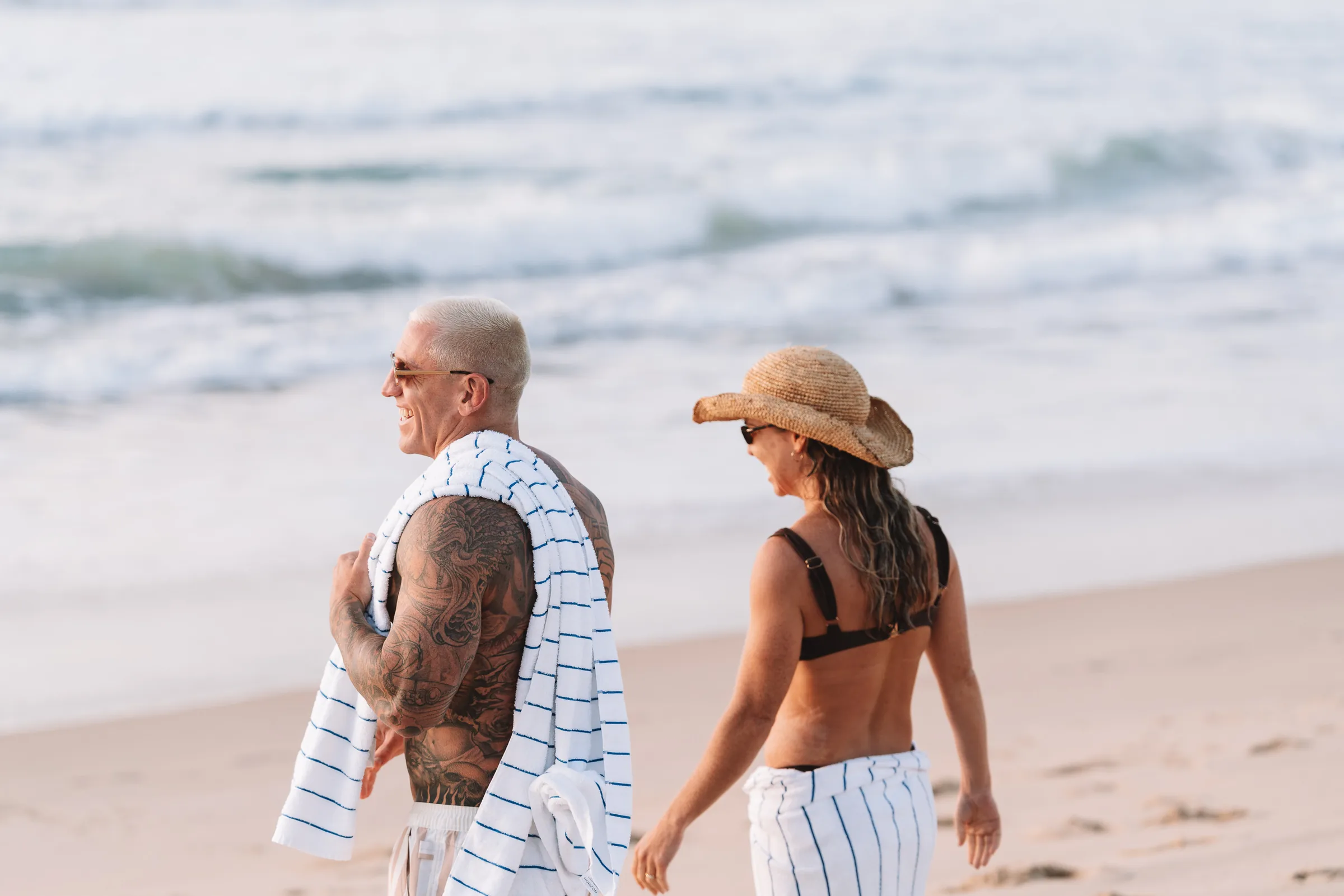 Two people on the sand with a towel, the surf behind them
