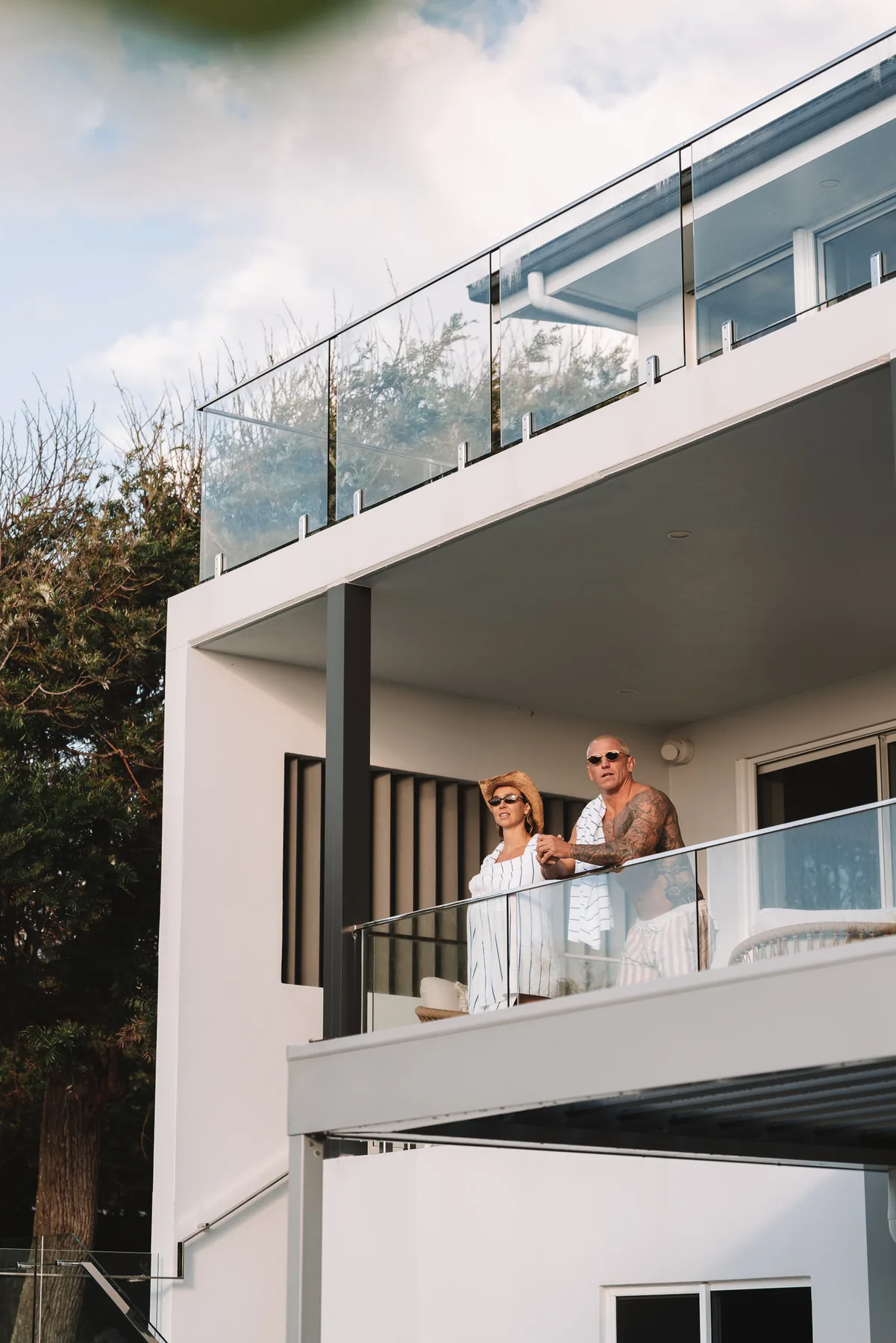 Two people on the upstairs balcony of a beach house, looking out