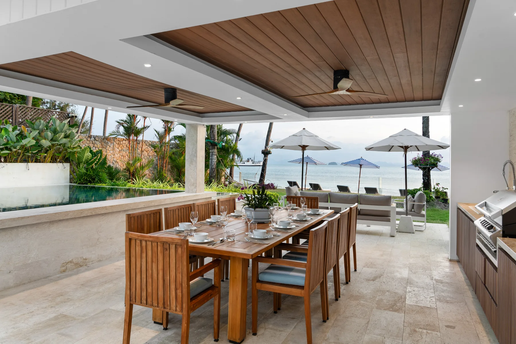 A long timber dining table set under a covered terrace