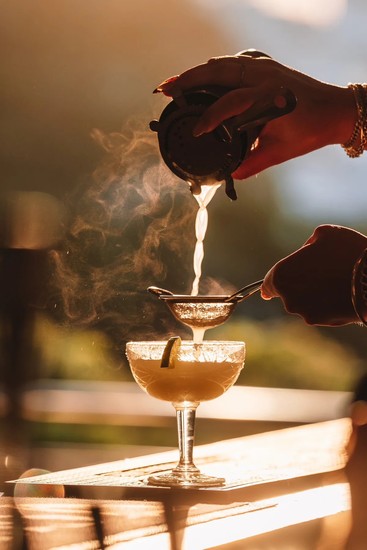 A cocktail being poured into a coupe glass