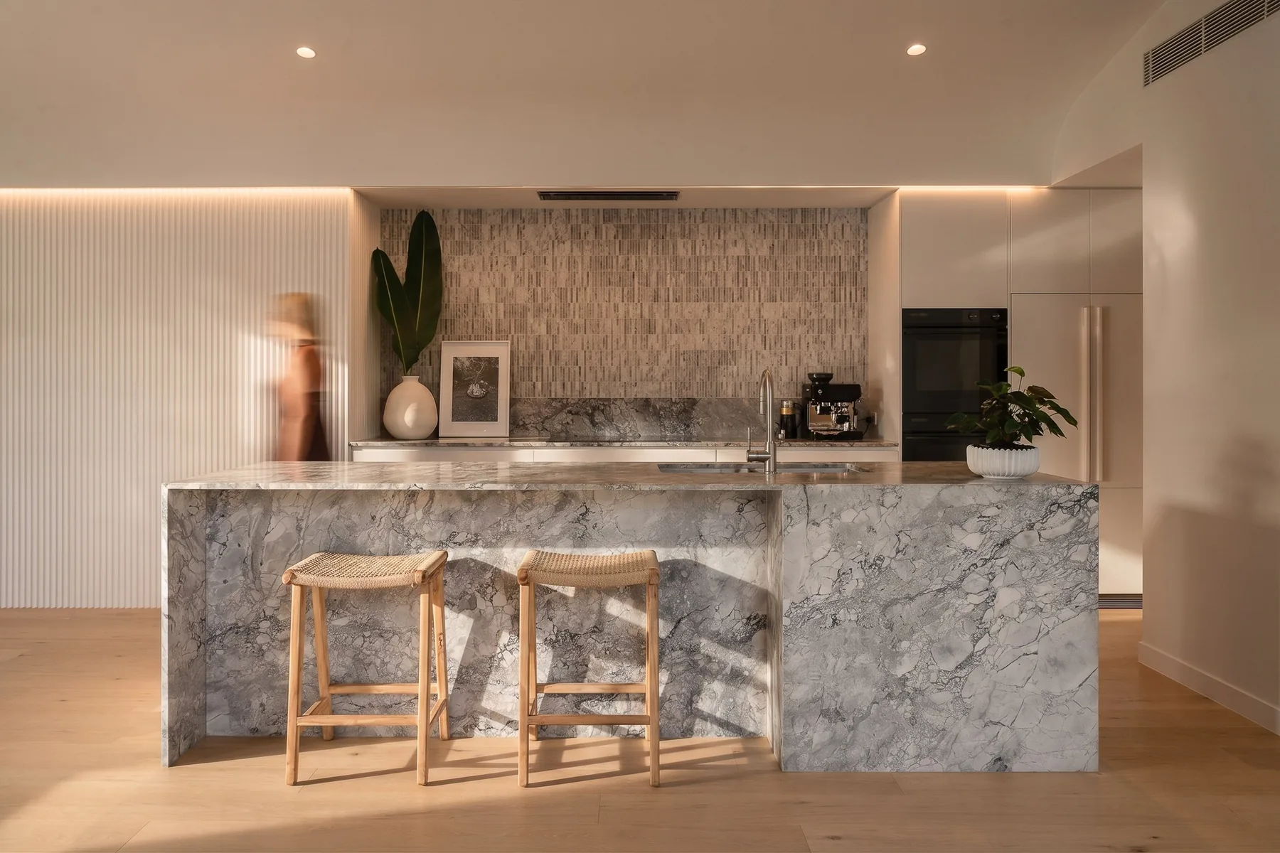 A marble kitchen island with stools and a fireplace beyond